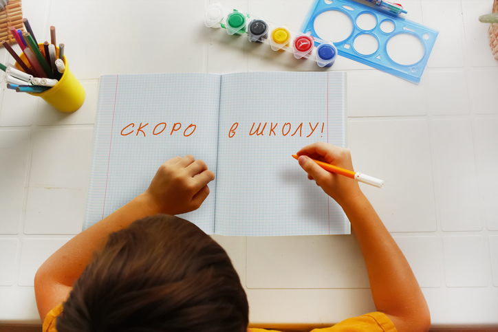 The boy writes in a notebook: soon to school, text in Russian. Back to school.