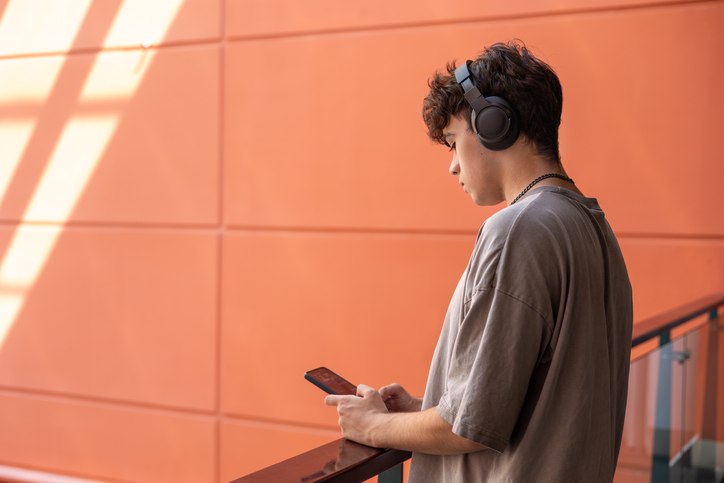 Teenager with headphones looking at smartphone, modern youth lifestyle, technology addiction, social media, online communication, emotions, stress, music listening. Copyspace