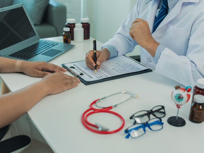 An ophthalmologist discusses how to correct a male patient's poor vision with a model of his eyeball and spectacles placed on a table.